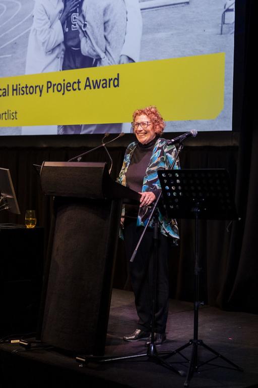 a woman standing at a podium on stage and speaking